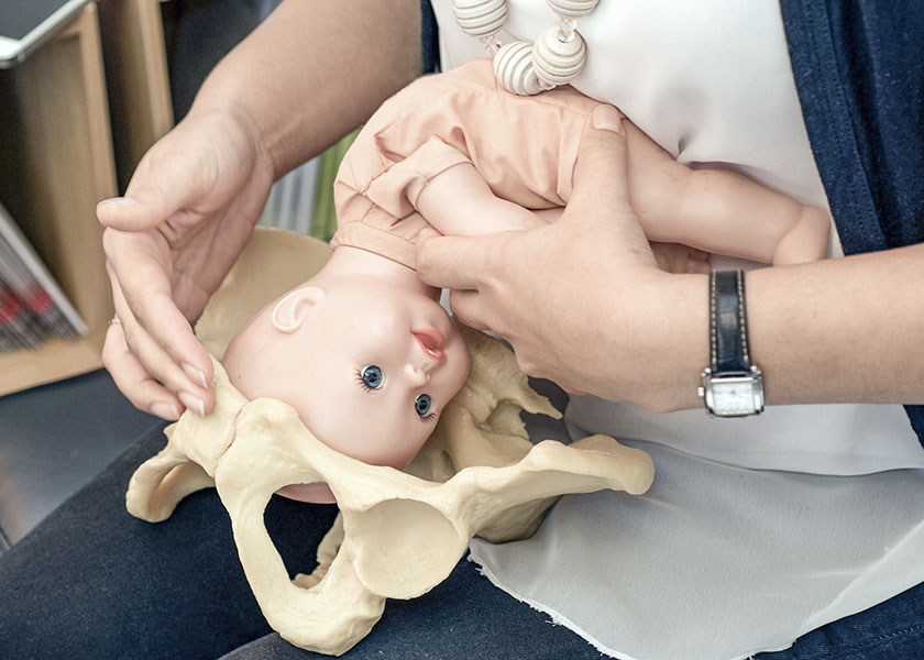 Photo d'une sage-femme en train d'expliqué un accouchement avec un bassin en plastique et une poupée de bébé